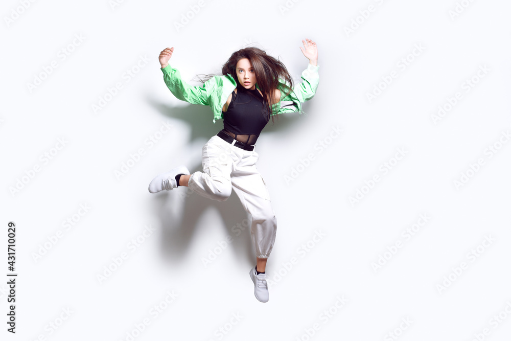 A girl dances in a green jacket a beating light, a fashionable teenager moves, laughs, dances, a party. Brunette with long hair. Girl in flight, jumping.