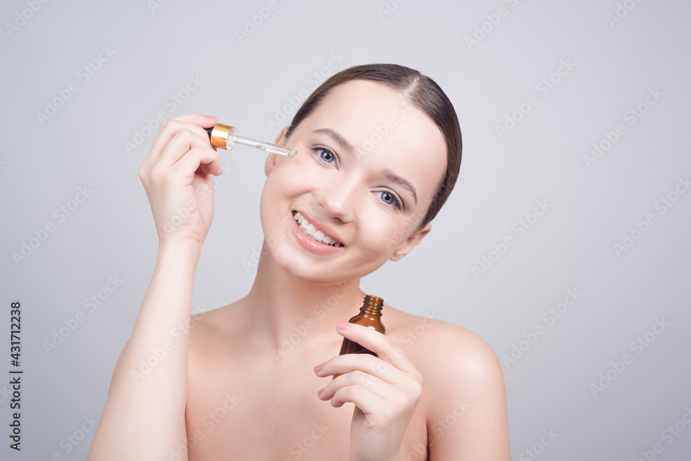 Obraz premium Close up of pretty brunette lady applying cosmetic oil on her face with pipette. Beauty therapy concept. Clean skin and face care. Youth and cosmetics