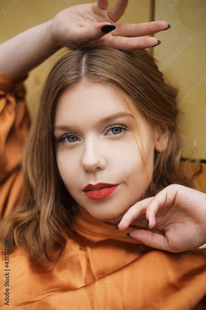 Fototapeta premium Portrait of a girl with short hair and red lips. Beautiful model with blue eyes in a fashionable brown dress. Model posing against the wall. Gorgeous short hair.