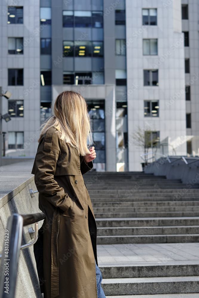 Fototapeta premium Woman stands against a business center. Young businessperson near an office building in the financial district of the city. Urban concept. Walk in a modern city.