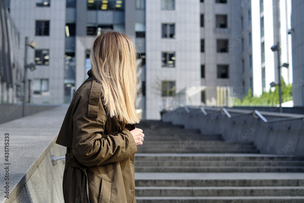 Fototapeta premium Woman stands against a business center. Young businessperson near an office building in the financial district of the city. Urban concept. Walk in a modern city
