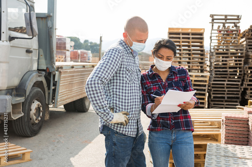 Man worker and woman order picker in face masks collecting order in the warehouse of building materials