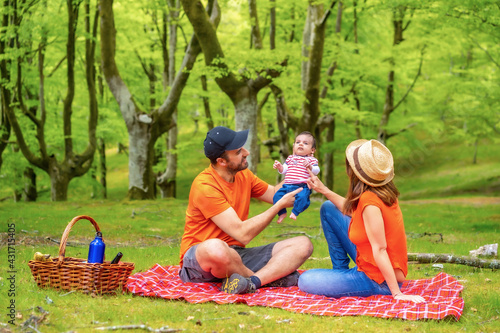 A picnic day with your newborn son. Dressed in orange t-shirts and hats, summer lifestyle of a family on vacation