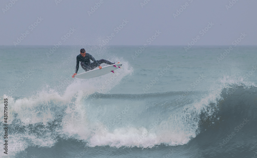 Surfer doing an aerial on a cloudy day with a nice bluish wave Surfer doing an aerial on a cloudy day with a nice bluish wave