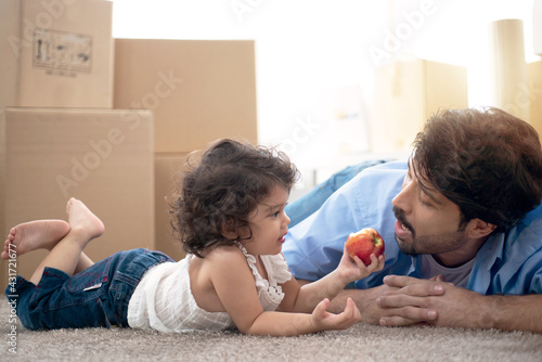 Father and daughter lying on the floor, after move into a new home, cardboard boxes for moving at room in background, daughter feeds apple for dad, father's day © chomplearn_2001