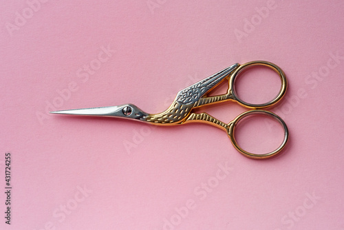 Scissors in the form of a bird made of gold and silver on a pink background.