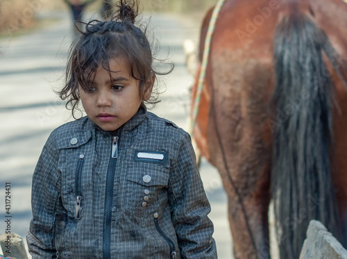 Beautiful sad little gypsy girl in a Roma settlement on blurred background of a horse 