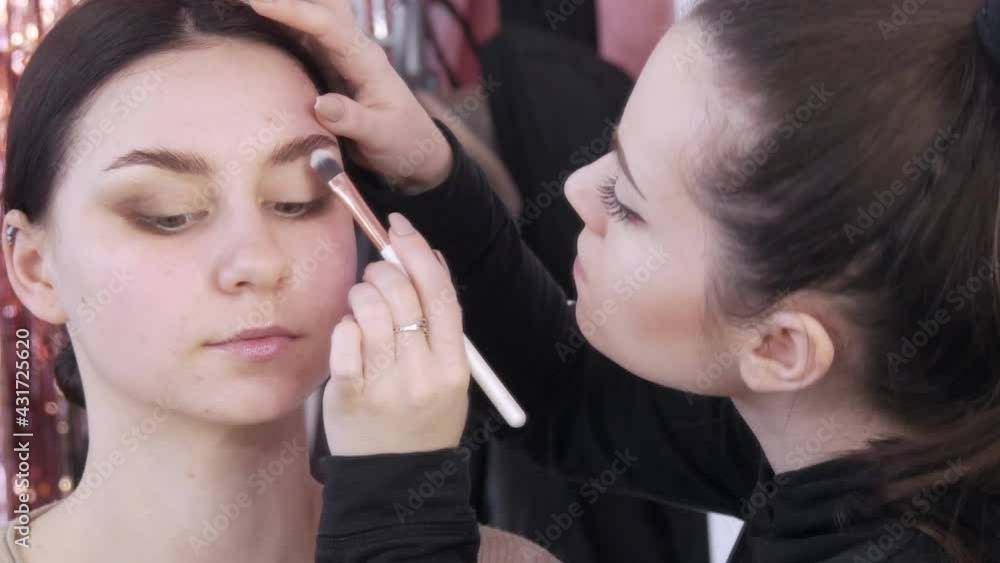 The stylist make-up master makes an eye on the evening stylish bright makeup on a young girl model in a beauty studio, a special brush paints with eye shadows using a special brush The stylist make-up master makes an eye on the evening stylish bright makeup on a young girl model in a beauty studio, a special brush paints with eye shadows using a special brush
