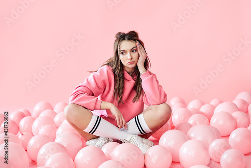 Bored fashionable woman sitting on floor with pink air balloons on pink pastel background © GVS