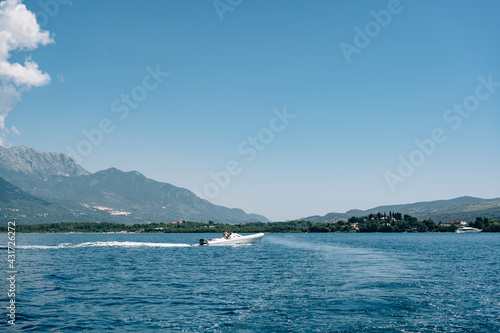 Tourists ride on white. sports boat in the sea against the backdrop of mountains in Montenegro. The concept of rich life and travel around the world. © Nadtochiy