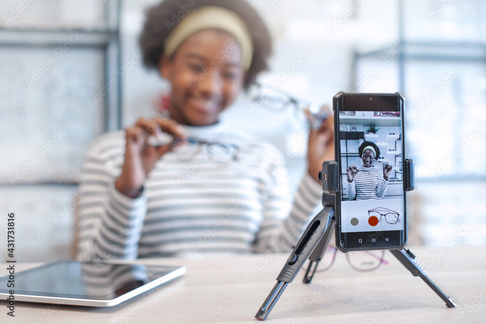 African blogger influencer recording video blog speaking and looking at  smartphone on tripod at optical store, recording and share on social media  live streaming Internet, selective focus Stock Photo | Adobe Stock