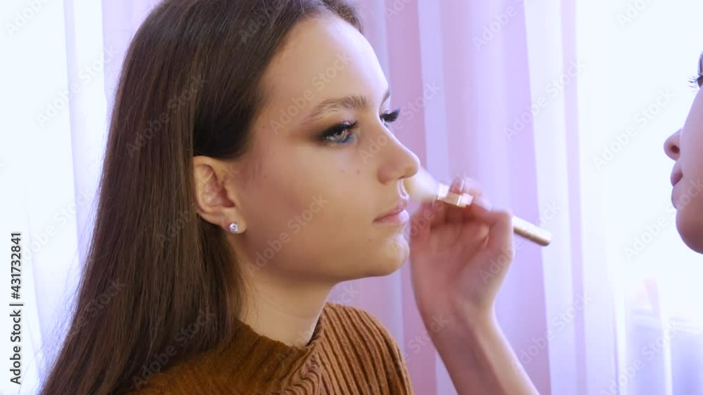 The stylist make-up master applies a foundation or concealer on the face of a young girl model using a special brush The stylist make-up master applies a foundation or concealer on the face of a young girl model using a special brush