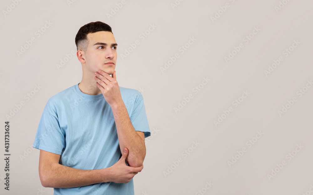 Pensive young guy thinking over problem, making decision, looking at blank space over grey studio background Pensive young guy thinking over problem, making decision, looking at blank space over grey studio background