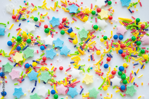 Multi-color festive background of a scattering of sugar candy sprinkles for cupcakes and other pastries in form of stars, sticks and balls. Bright colors of red, pink and green, blue and yellow
