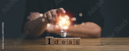 Foto hand touching on light bulb on wood block with Word Ideas, new idea concept with innovation and inspiration, innovative technology in science and communication concept