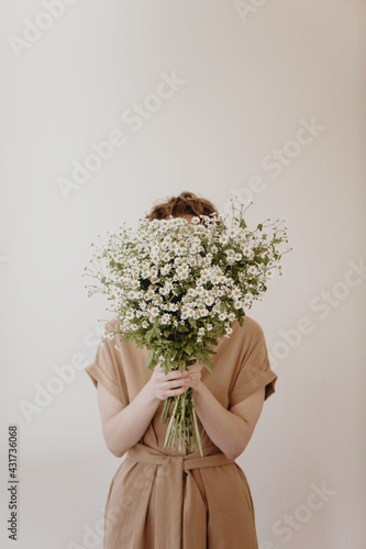 Fényképezés Woman hiding behind a bunch of daisies on white background.