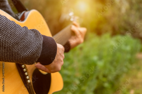 Closeup view of unrecognizable man playing acoustic guitar outdoors in nature at sunset.