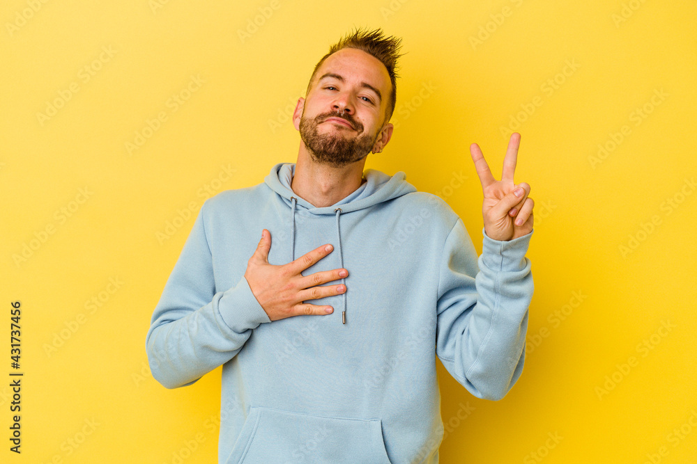 Young tattooed caucasian man isolated on yellow background taking an oath, putting hand on chest. Young tattooed caucasian man isolated on yellow background taking an oath, putting hand on chest.