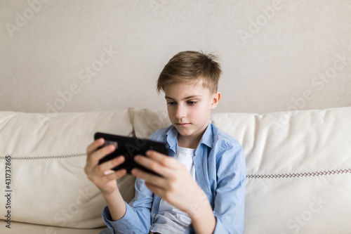 Child sit on the couch in his hands holding a phone, plays with it.