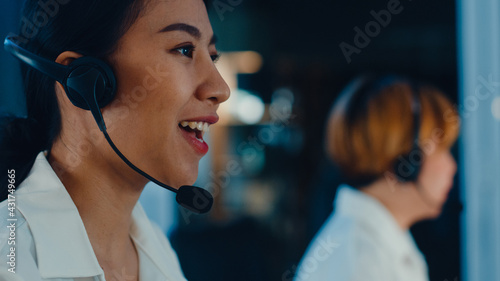 Millennial Asia young call center team or customer support service executive using computer and microphone headset working technical support in late night office. Telemarketing or sales job concept.