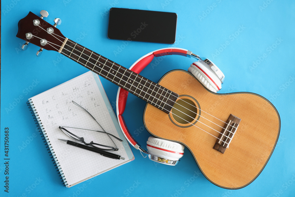 Fototapeta premium Guitar with headphones smartphones and notebook on blue background