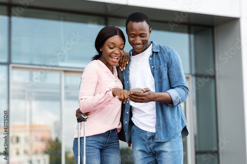Vászonkép Black travellers couple using smartphone outdoors, standing near airport buildin