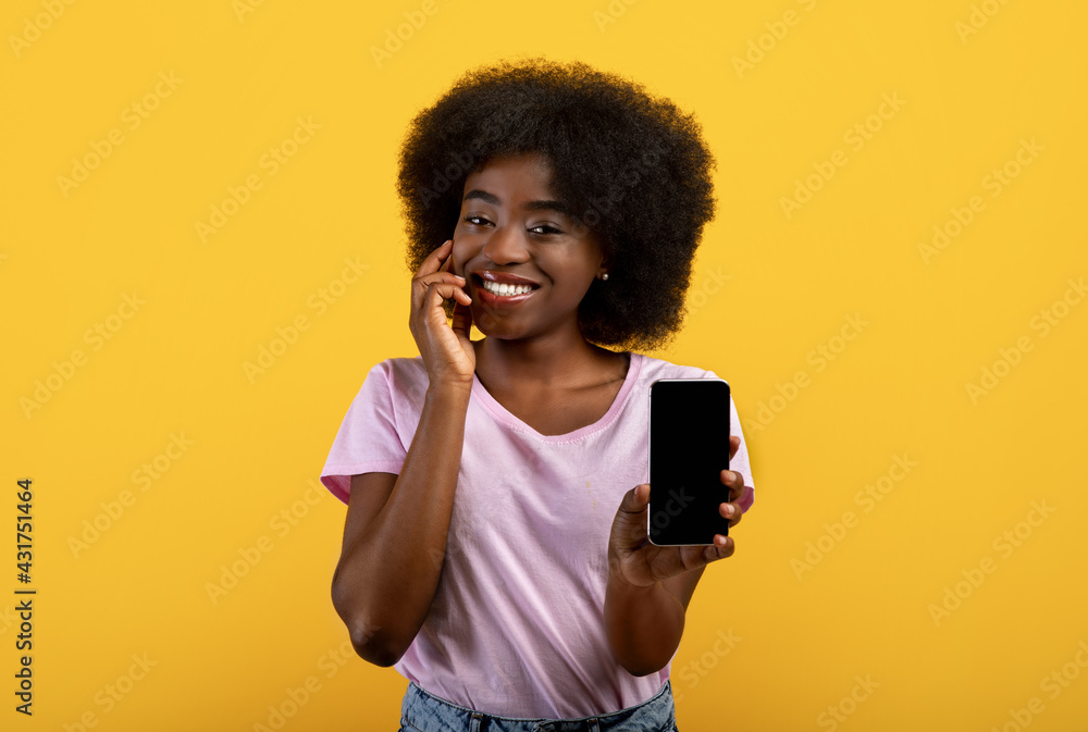 Pretty african american bushy woman showing smartphone with empty screen, advertising new app on yellow background Pretty african american bushy woman showing smartphone with empty screen, advertising new app on yellow background