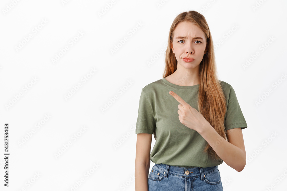 Obraz premium Not so sure. Skeptical young woman smirk and frown from doubts, pointing left at something average, judging bad promo deal, standing over white background