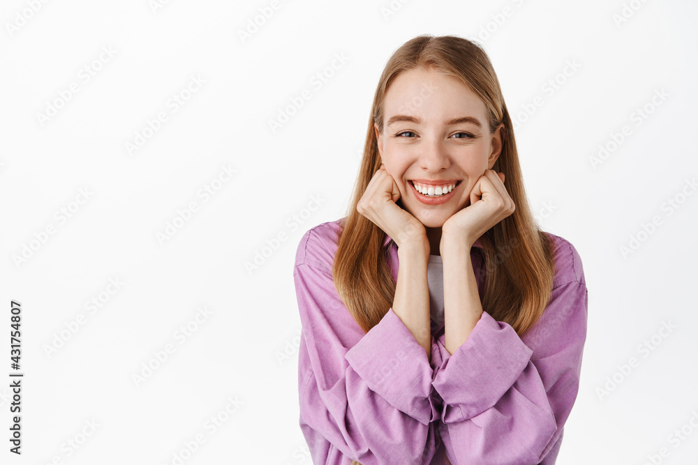Beautiful blond girl touching face, looking at something adorable, contemplating cute romantic thing, smiling happy, standing over white background Beautiful blond girl touching face, looking at something adorable, contemplating cute romantic thing, smiling happy, standing over white background
