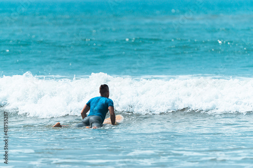 Surfer z deską w wodzie, czekający na nadchodzącą fale, mężczyzna uprawiający sport wodny. © insomniafoto