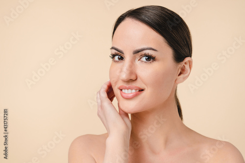 Young pretty caucasian woman touching her face with her hand isolated over beige background. Clean skin and beauty concept. Beautification, skin care, make-up and spa. Cosmetology.