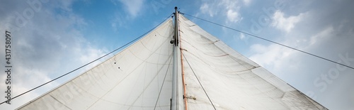 Vászonkép White sails of a sloop rigged yacht against cloudy blue sky