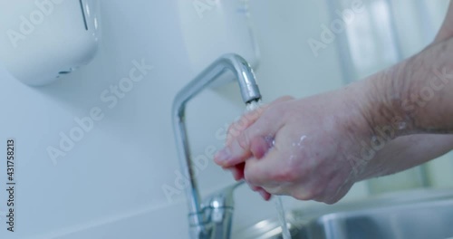 From the tap is pouring water and near somebody is lathering hands. photo