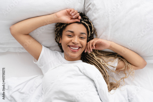 Lazy happy smiling young african woman lying in her white bed in the morning. Pretty African American woman waking up at home.