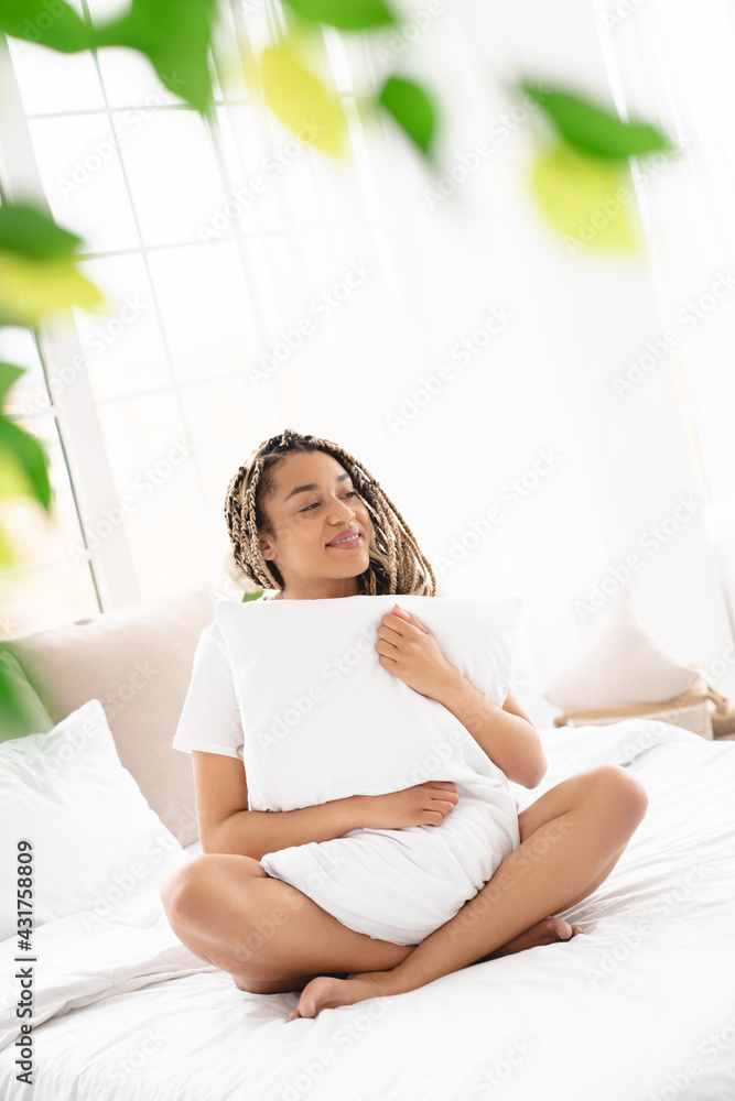 Vertical portrait of an afro young woman hiding behind the pillow ,relaxing on the comfy bed with white linen before getting up Vertical portrait of an afro young woman hiding behind the pillow ,relaxing on the comfy bed with white linen before getting up