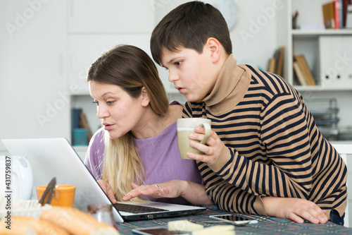 Portrait of young woman and son chatting at table with laptop indoors