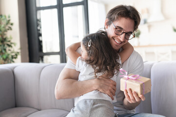 Happy caring loving little girl daughter embracing hugging her young father giving him a present for father`s day or birthday, congratulating him. I love you, dad! Parenthood, fatherhood