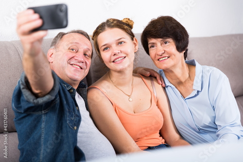 Marrieds with their adult daughter are takinf selfie together on sofa indoor. photo