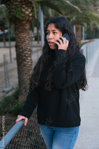 Worried young latin girl doing a phone call. Woman receiving bad news by phone. Model outdoors calling.