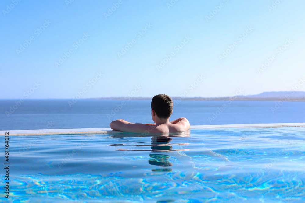 a young guy is resting on the edge of a blue pool overlooking the sea. summer vacation concept