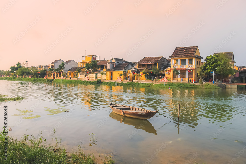 Obraz premium A lone traditional Vietnamese boat on Thu Bon River during a golden sunset in the quaint old town village Hoi An, Vietnam.