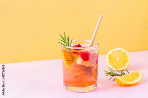Trendy exotic summer drink with disposable paper straw and rosemary on bicolor background (pink and orange). Fresh fruit lemonade with raspberry for vegans. Copy space