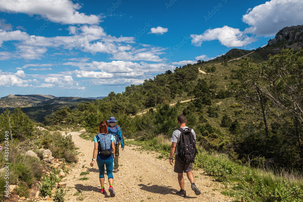 Hikers walking down a country road, with a cloudy blue sky in the background.