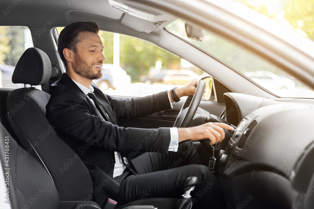 Handsome businessman driving car to airport, turning on music