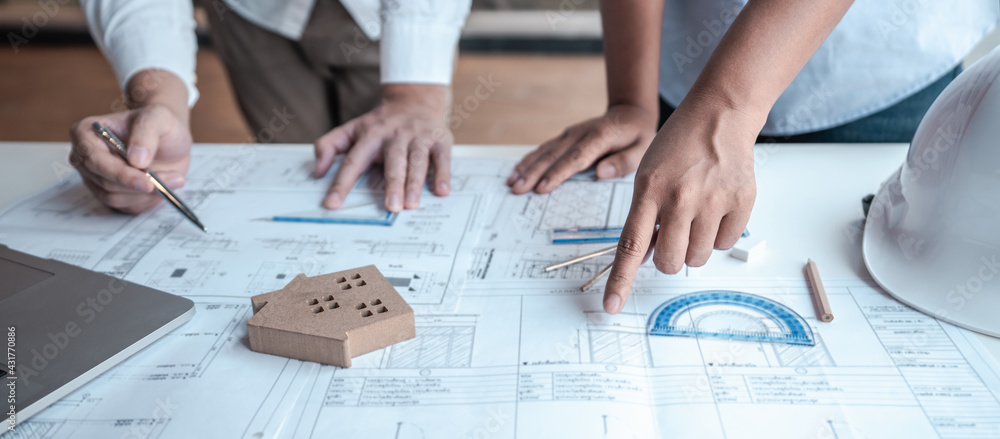 Team of architects or engineering consulting and analyzing working on objects tools and construction drawings inspection, discussing planning new architectural project on blueprint and model house Team of architects or engineering consulting and analyzing working on objects tools and construction drawings inspection, discussing planning new architectural project on blueprint and model house