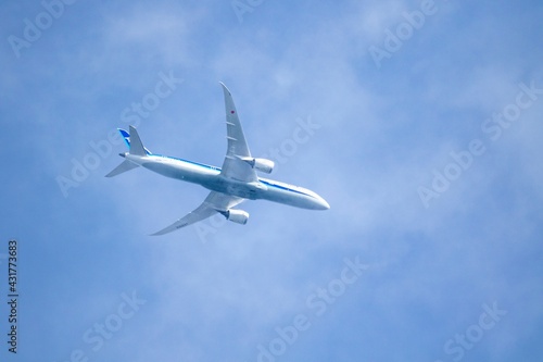 A portrait of a touristic airplane flying through a thin cloud in a blue sky at daytime. The airplane is blue and white and is carrying people to their touristic vacation or business trip.