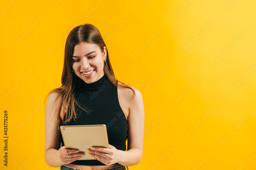 Attractive brunette young woman using tablet computer and smiling, isolated on yellow background in studio with copy space. Attractive brunette young woman using tablet computer and smiling, isolated on yellow background in studio with copy space.
