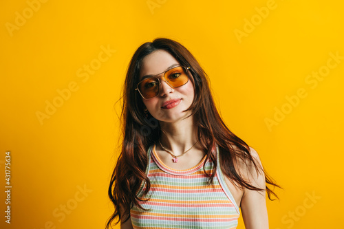 Portrait of attractive stylish woman in sunglasses with long brunette hair isolated on yellow background in studio.
