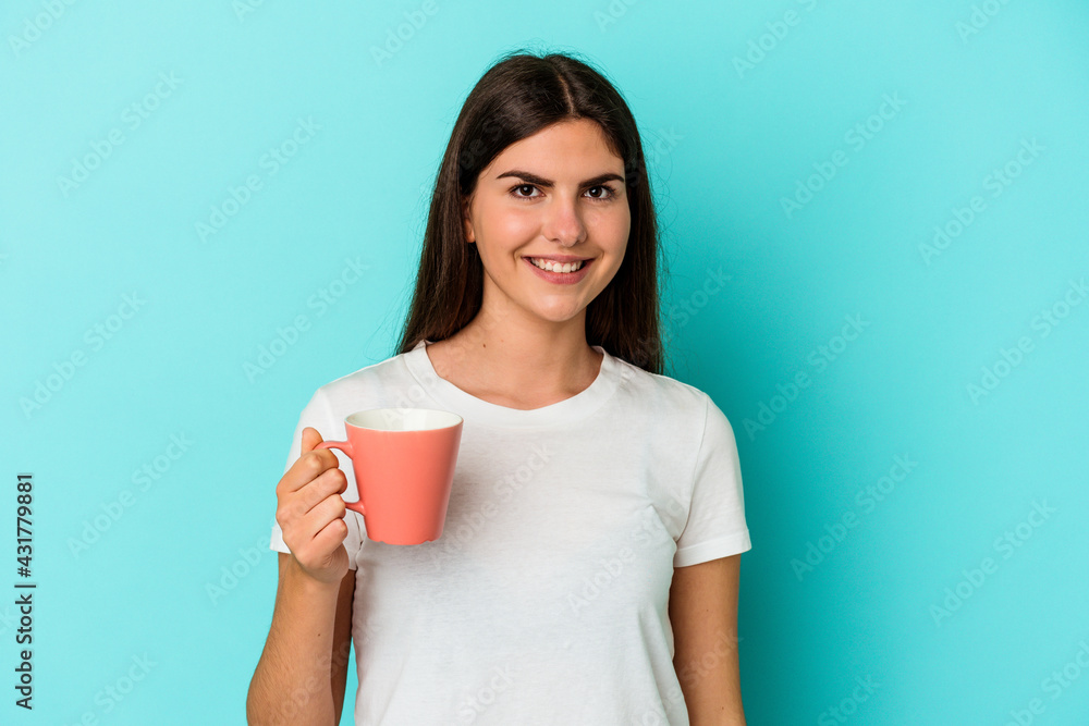Young caucasian woman holding a mug isolated on blue background happy, smiling and cheerful. Young caucasian woman holding a mug isolated on blue background happy, smiling and cheerful.