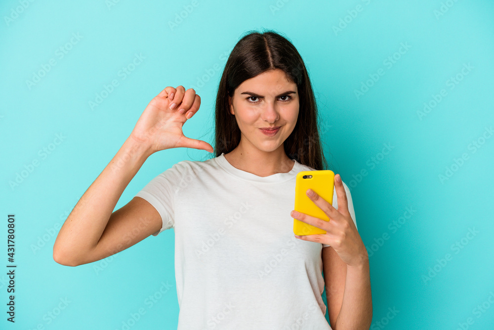Young caucasian woman holding a mobile phone isolated on blue background feels proud and self confident, example to follow. Young caucasian woman holding a mobile phone isolated on blue background feels proud and self confident, example to follow.
